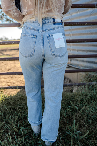 Person wearing light blue jeans with a brand label, standing in a field.