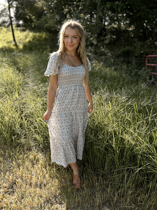 Woman in a floral dress standing in a grassy field with trees in the background