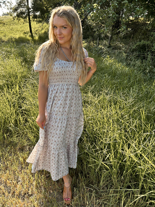 Woman in a floral dress standing in a grassy field with trees in the background