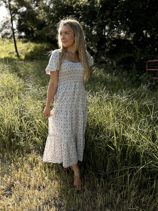 Woman in a floral dress standing in a grassy field with trees in the background