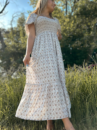 Woman wearing a floral dress standing in a natural setting with trees and grass.