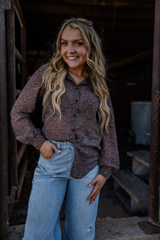 Woman wearing a patterned shirt and jeans standing in a rustic setting