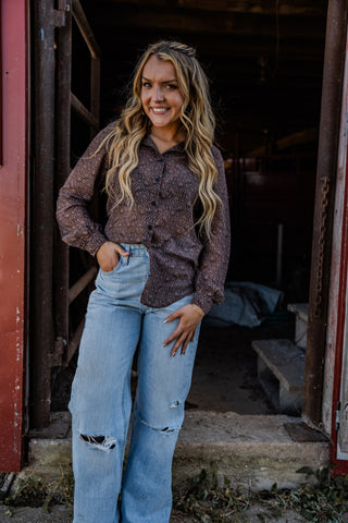 Woman wearing a patterned shirt and light blue jeans standing in an open doorway.
