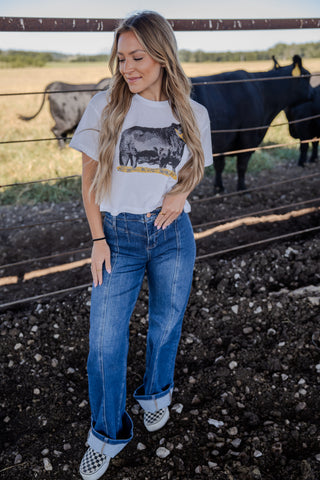 Woman wearing a graphic t-shirt and jeans standing near a fence with cows in the background