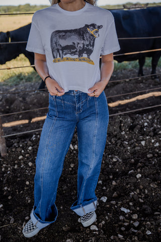 Person wearing a t-shirt with a cow graphic in an outdoor setting with animals in the background