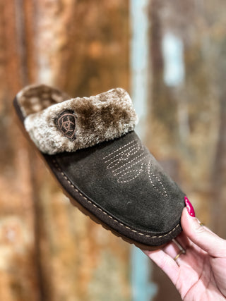 Brown slipper with fur lining held by a hand against a blurred natural background