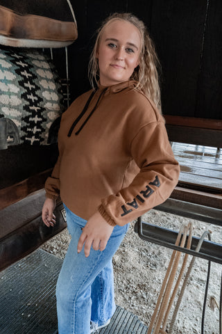 Woman wearing a brown hoodie with text on the sleeves in an indoor setting.