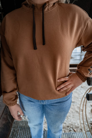 Person wearing a brown hoodie and blue jeans standing outdoors.