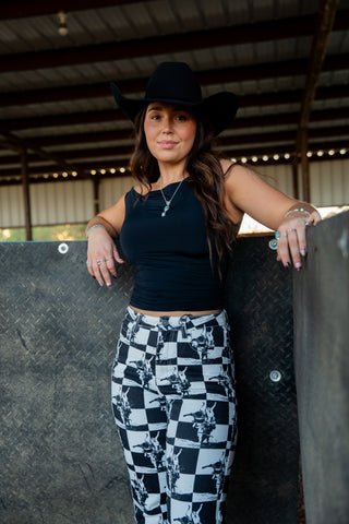 Woman wearing a black top and checkered pants standing against a metallic wall.
