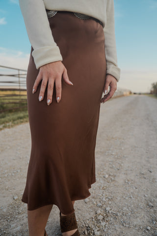 Person wearing a brown skirt standing on a gravel road with a blurred background