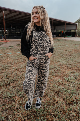 Woman wearing leopard print overalls and black sneakers in an outdoor setting.
