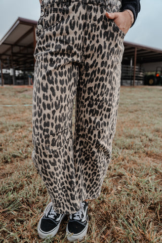Person wearing leopard print pants and black sneakers standing on grass.