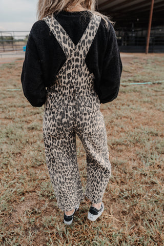 Person wearing leopard print overalls and a black jacket in an outdoor setting