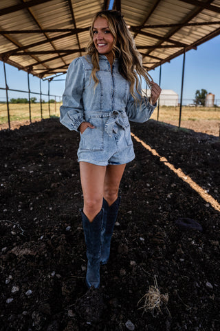 Woman in denim outfit standing in a barn with a field in the background