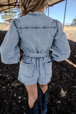 Person wearing a denim romper with long sleeves in an outdoor setting