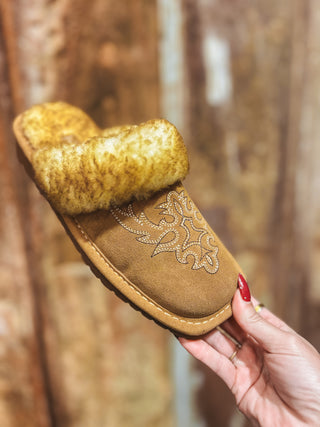 Brown slipper with fur trim held by a hand against a blurred background