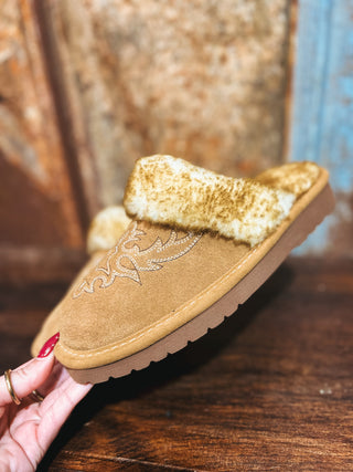 Brown slipper with fur lining held by a hand on a wooden surface