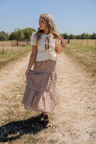 Woman in a patterned dress standing on a dirt path with trees in the background
