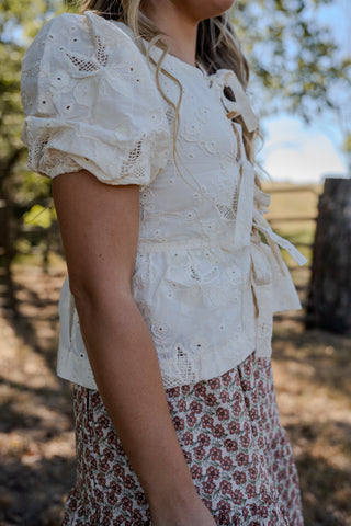 Person wearing a white lace top with ruffled details outdoors.