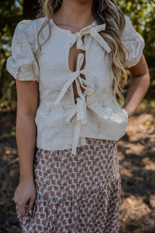 Woman wearing a white lace top with puff sleeves and a floral skirt outdoors.