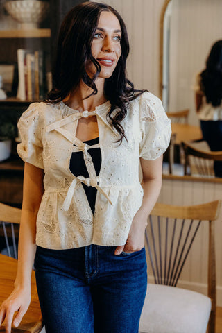 Woman wearing a beige lace top and blue jeans in an indoor setting