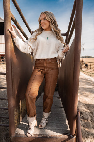 Woman in a white sweater and brown pants standing on a rustic metal staircase.