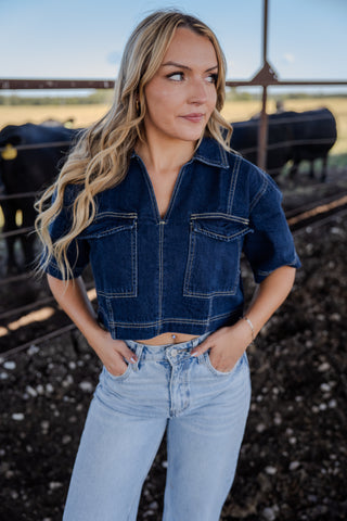 Woman wearing a denim jacket and jeans standing in a field.
