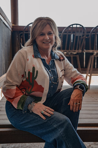 Woman wearing a colorful cardigan with a desert design, sitting indoors.