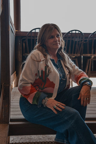 Woman sitting on a staircase wearing a colorful jacket with a cactus design.
