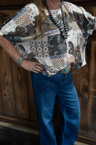 Person wearing a patterned blouse and blue jeans against a wooden background