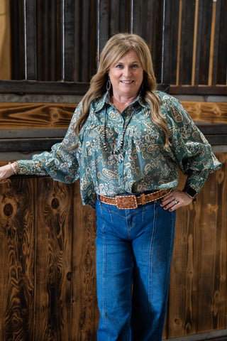 Woman in a patterned shirt and blue jeans standing against a wooden background