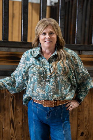 Woman wearing a patterned blouse and blue jeans standing in front of wooden panels.