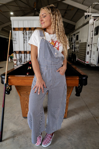 Woman in striped overalls standing in a garage with a pool table.