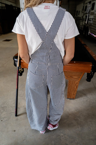 Person wearing a striped overalls and white shirt in an indoor setting