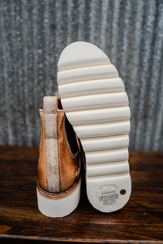 Brown leather shoe with white sole on a wooden surface