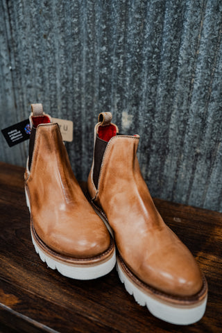 Pair of brown leather boots with white soles on a wooden surface.
