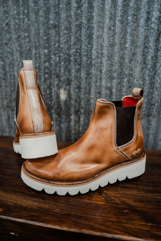 Brown leather boots with white soles on a wooden surface and textured gray background