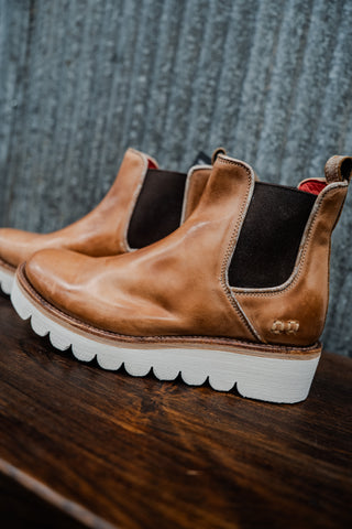 Brown leather boots with white soles on a wooden surface