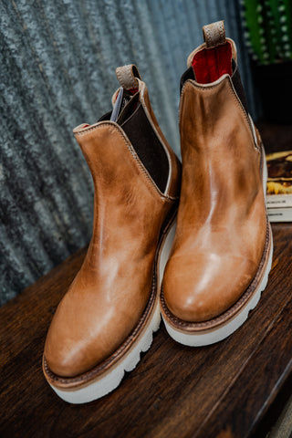 Pair of brown leather boots with white soles on a wooden surface.