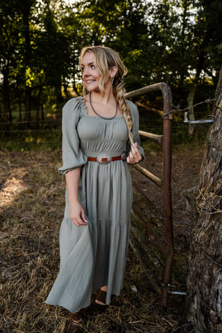 Woman in a gray dress standing in a field with trees in the background