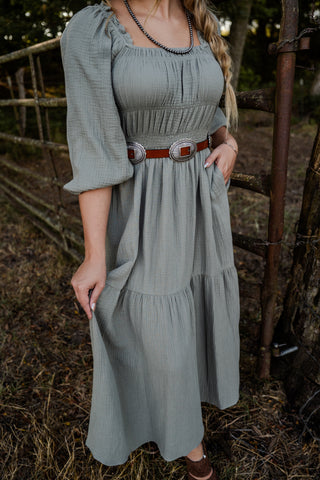 Woman wearing a green dress with a belt in a rustic outdoor setting