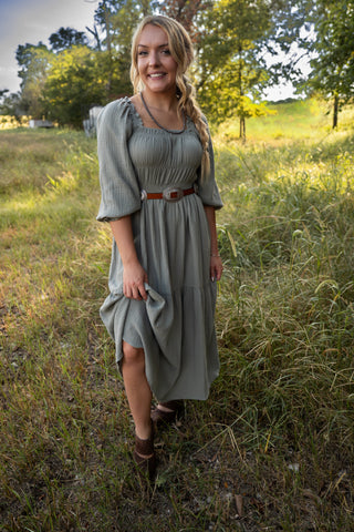 Woman in a green dress standing in a grassy field with trees in the background