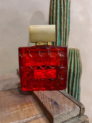 Red perfume bottle with gold cap on a wooden surface with a cactus in the background