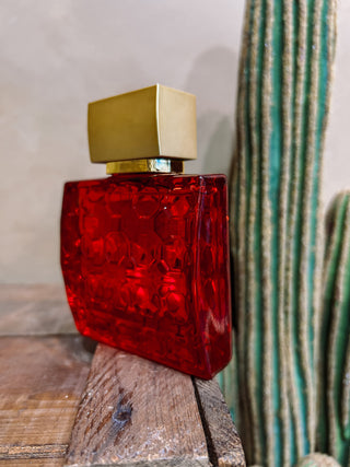 Red glass bottle with gold cap on a wooden surface next to a cactus