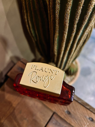Perfume bottle labeled 'Flaunt Rouge' with a cactus in the background