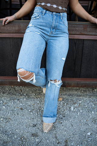 Person wearing ripped blue jeans sitting on a bench.