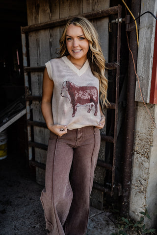Woman wearing a sleeveless sweater with a cow design in a rustic setting