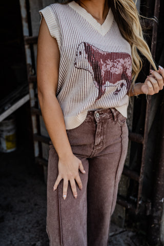 Person wearing a sleeveless top with a cow graphic and high-waisted brown pants in an indoor setting.