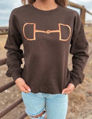 Person wearing a brown sweatshirt with a horse bit design outdoors.