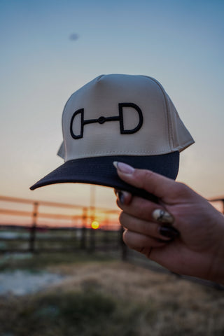 Hand holding a cap with a logo against a sunset background